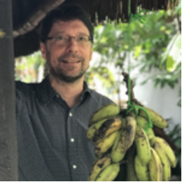 A person standing next to a bunch of bananasDescription automatically generated with medium confidence